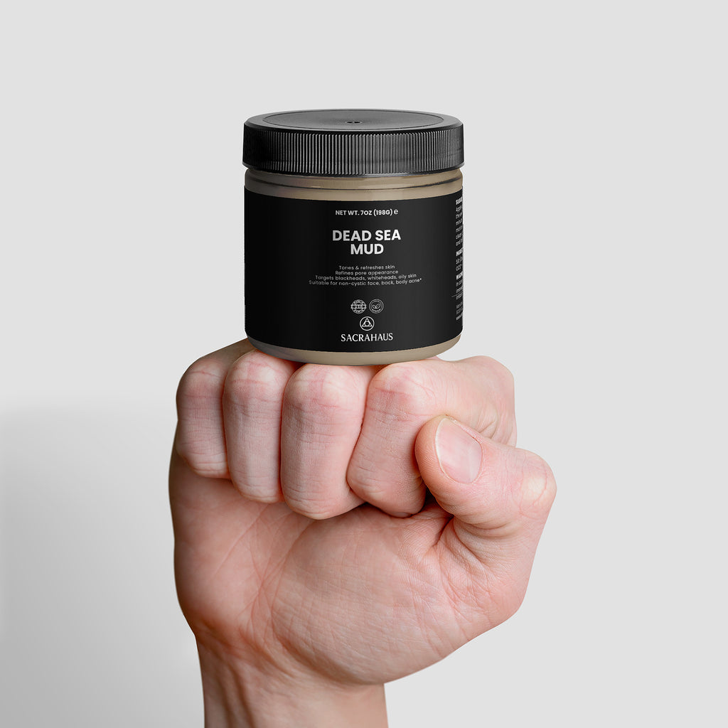 Hand holding SACRAHAUS Dead Sea mud mask in a sleek black jar for skin rejuvenation