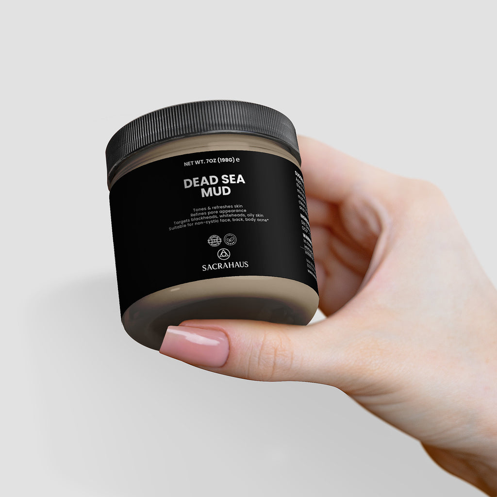 Hand holding SACRAHAUS Dead Sea mud mask in a stylish jar for rejuvenating skin care