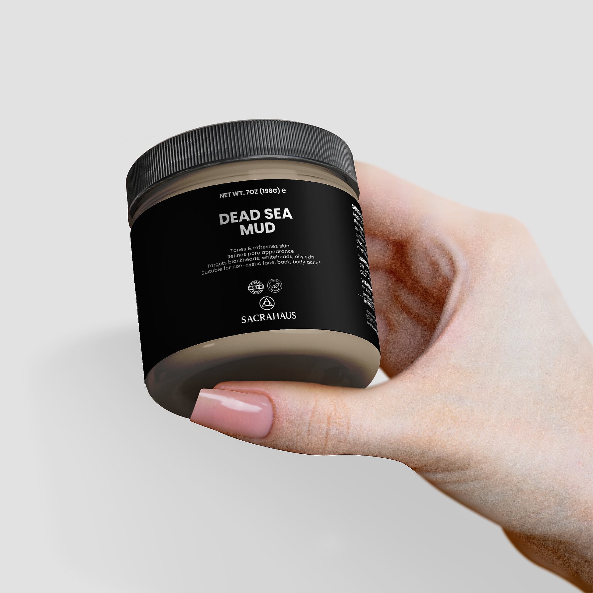 Hand holding SACRAHAUS Dead Sea mud mask in a stylish jar for rejuvenating skin care